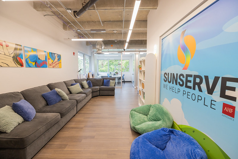 Modern lounge with sectional sofa, beanbags, and SunServe wall sign.